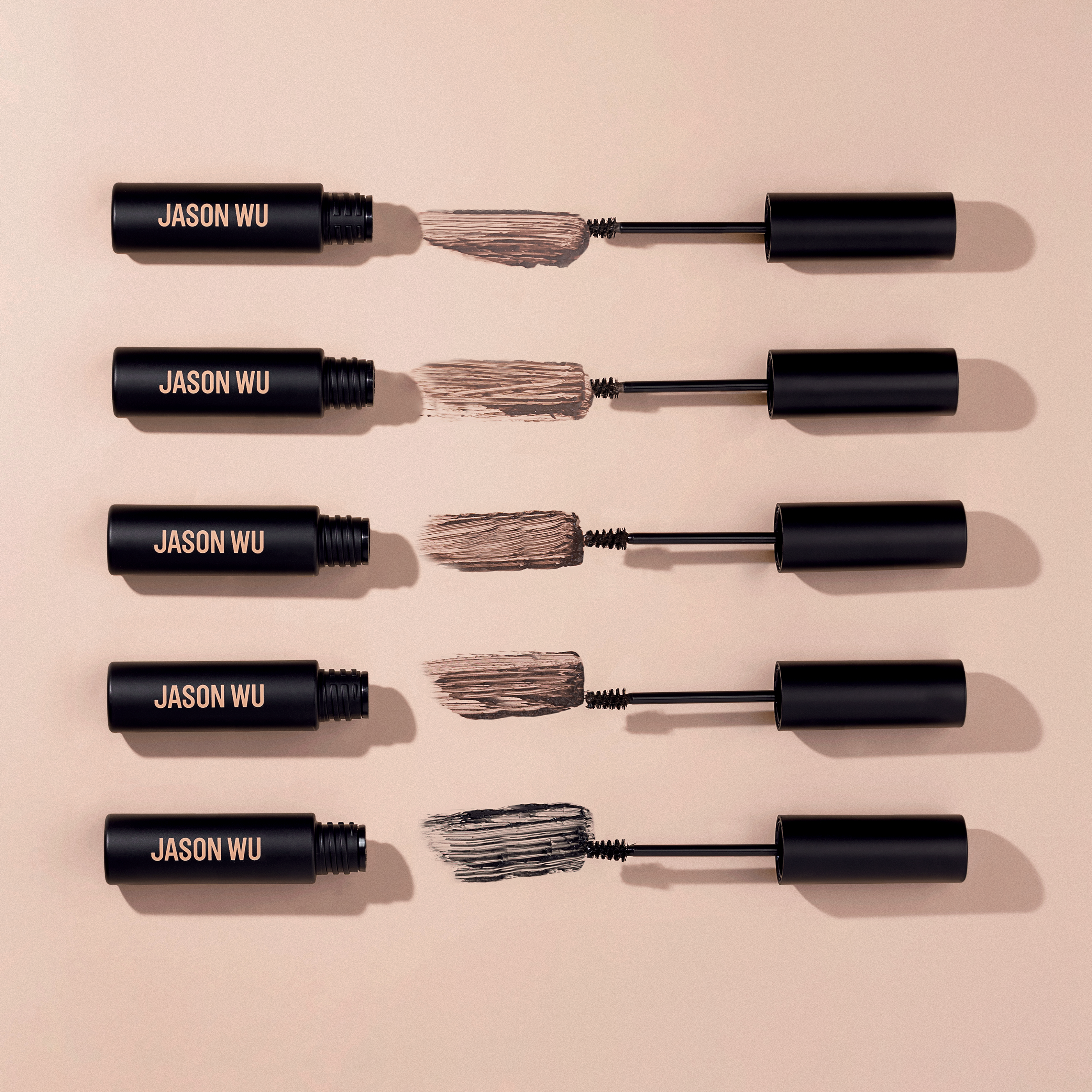 Five mascara tubes with brushes on a beige background.