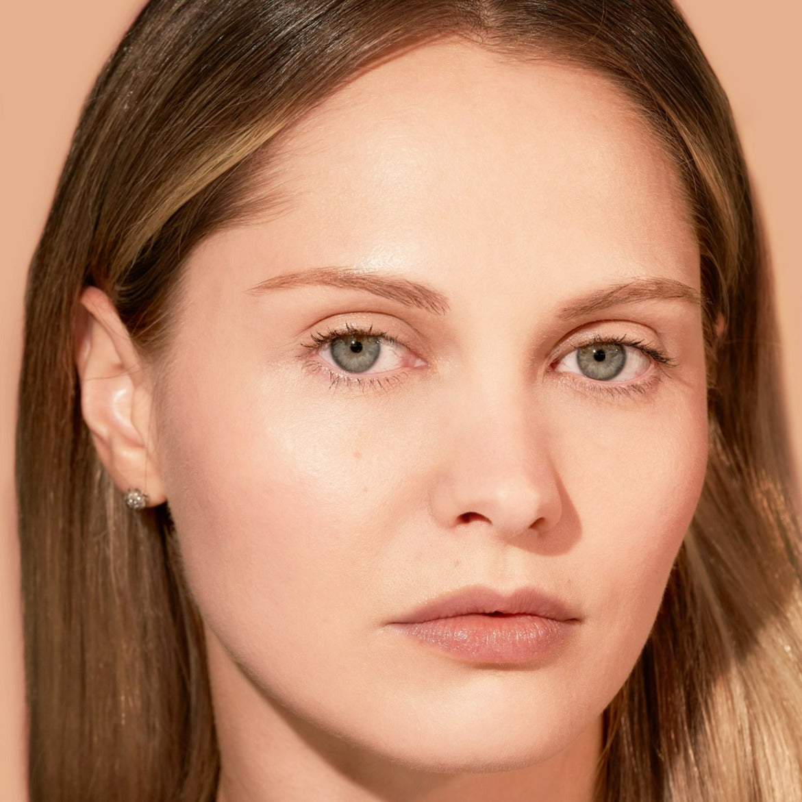 Close-up portrait of a woman with light skin and straight brown hair against a neutral background.