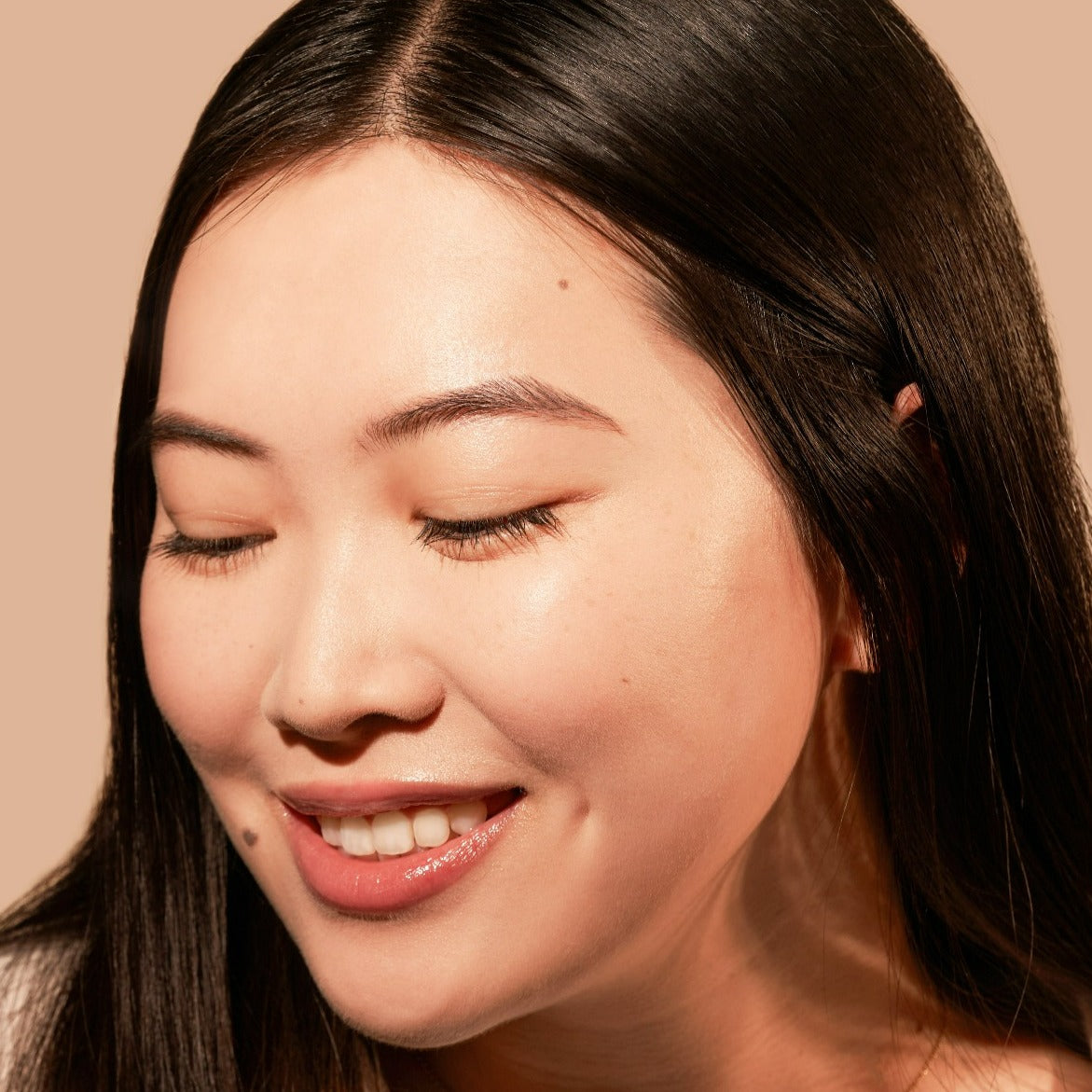 Woman smiling with eyes closed against a neutral background.