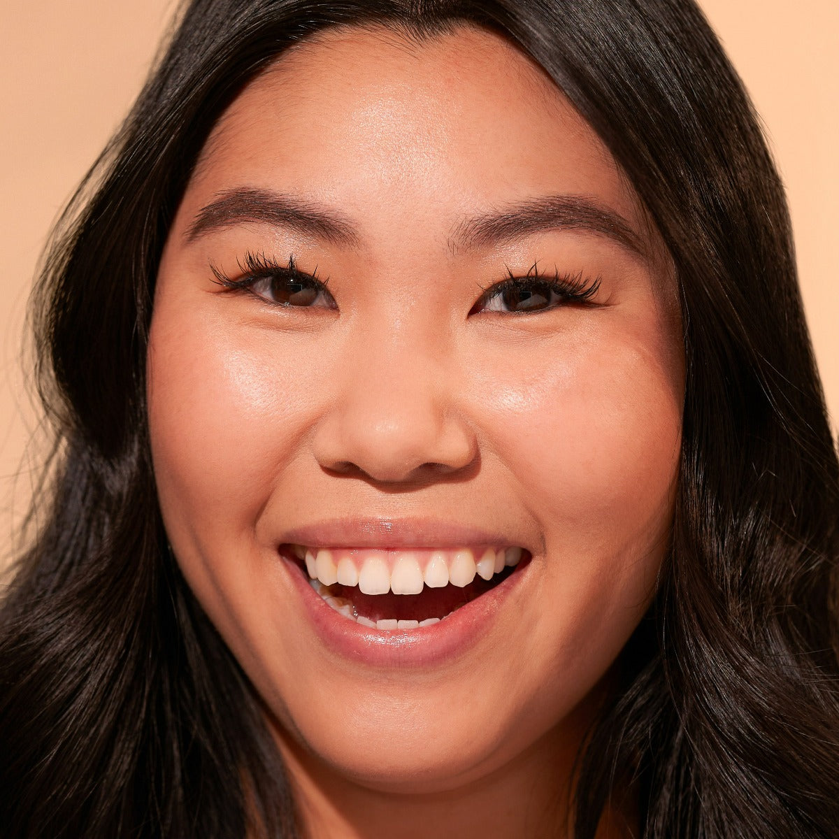 Close-up of a smiling person with long dark hair against a neutral background.