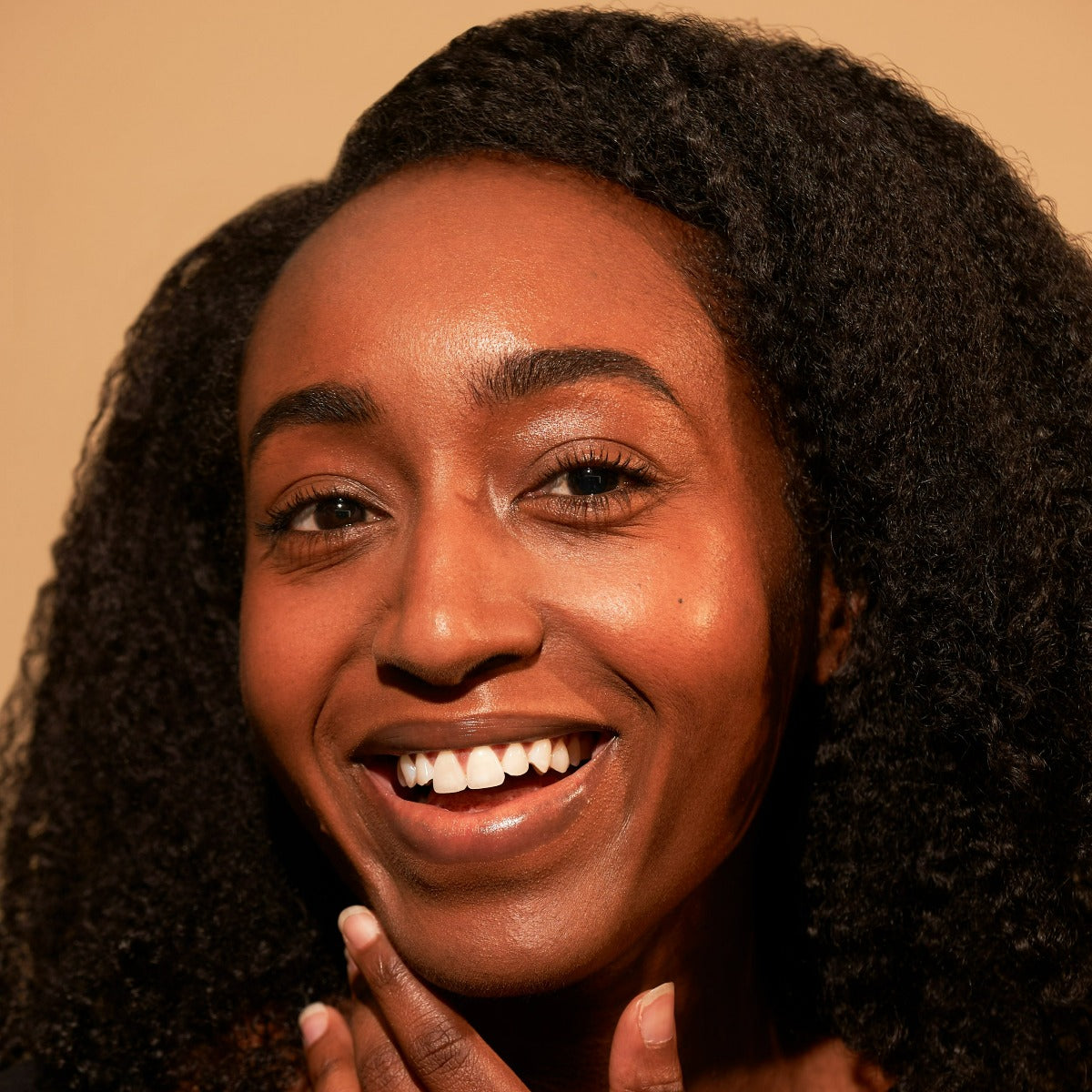 Smiling person with curly hair touching their face