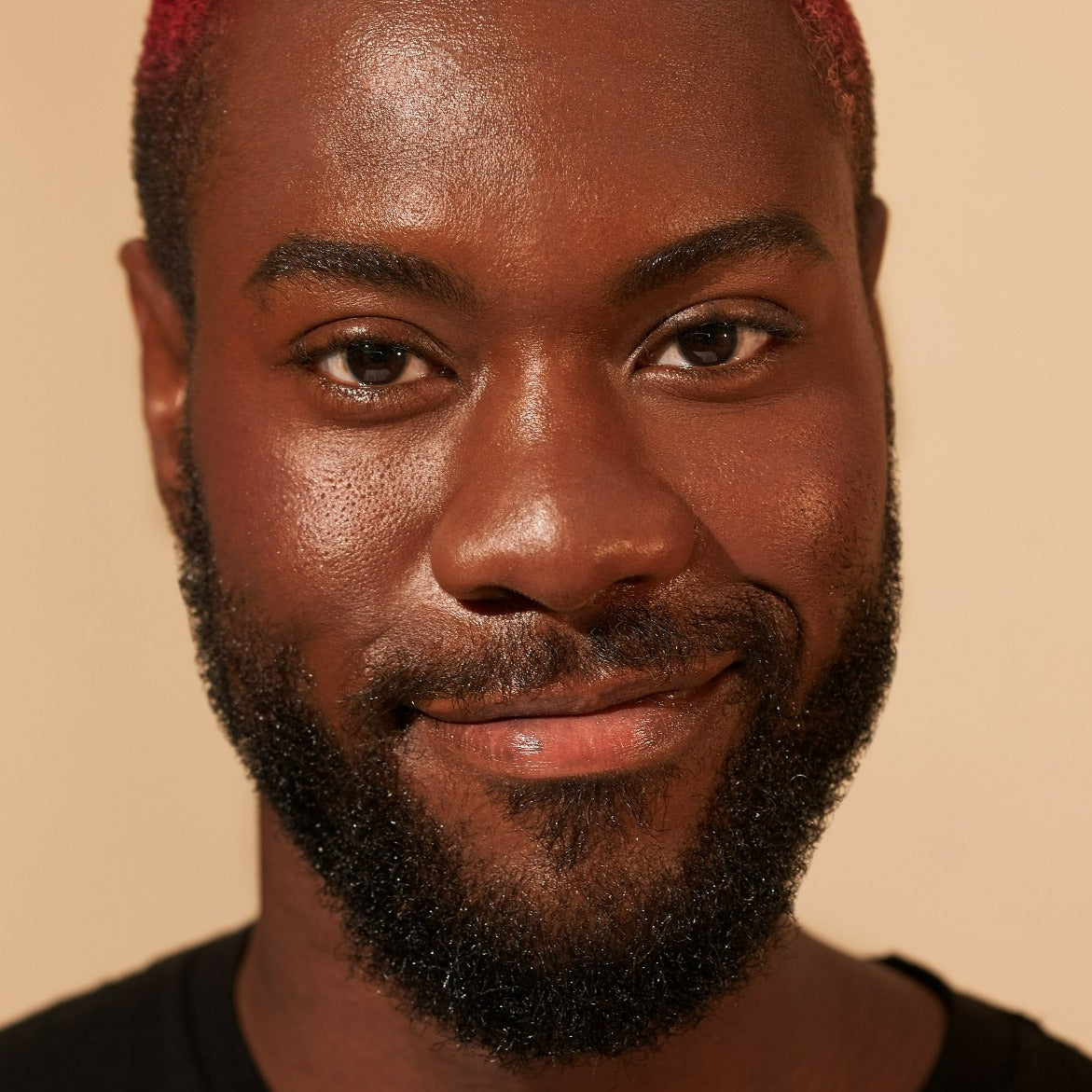 Portrait of a person with a beard and short hair smiling against a neutral background.