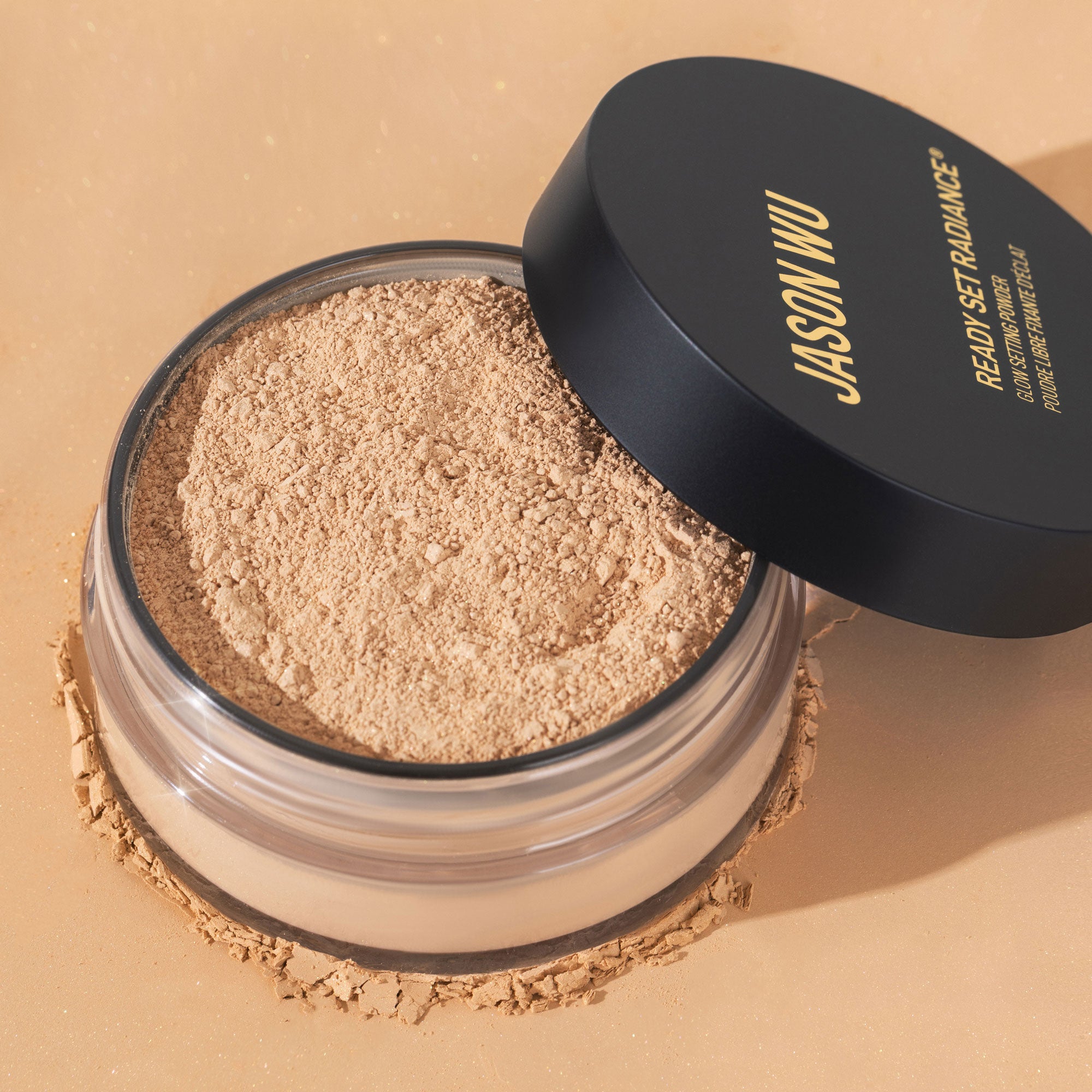 Open jar of loose face powder with black lid on a beige background.