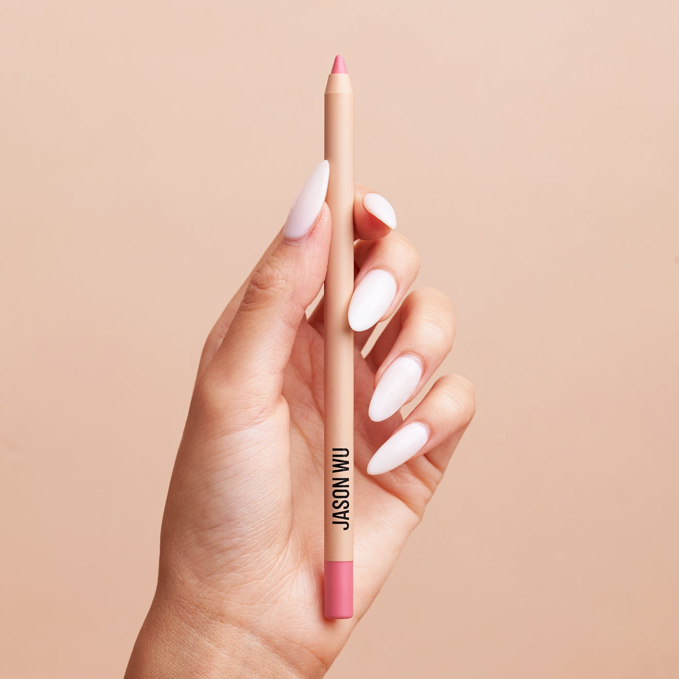 Hand holding a pink lip liner against a beige background.