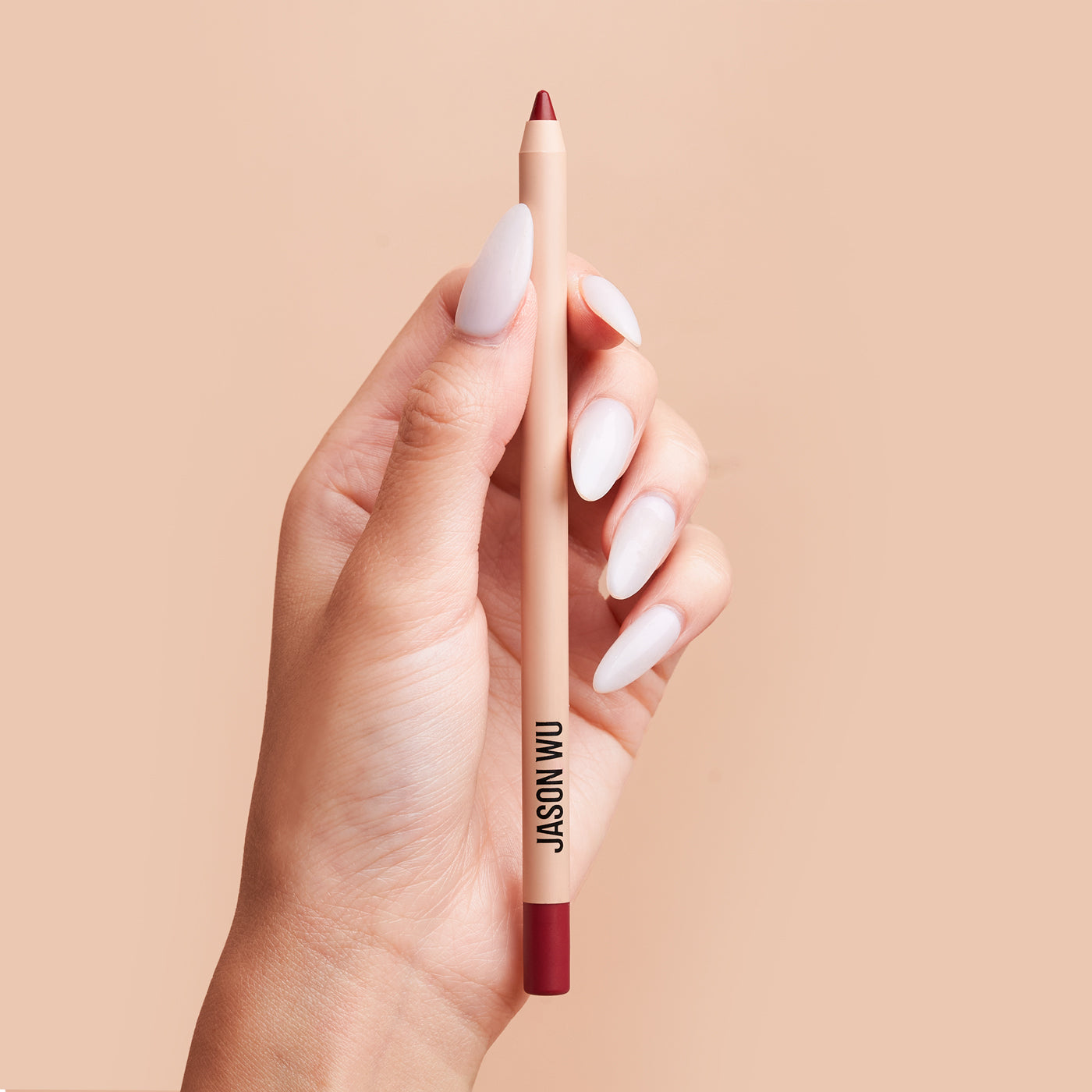 Hand holding a red lip liner against a beige background.