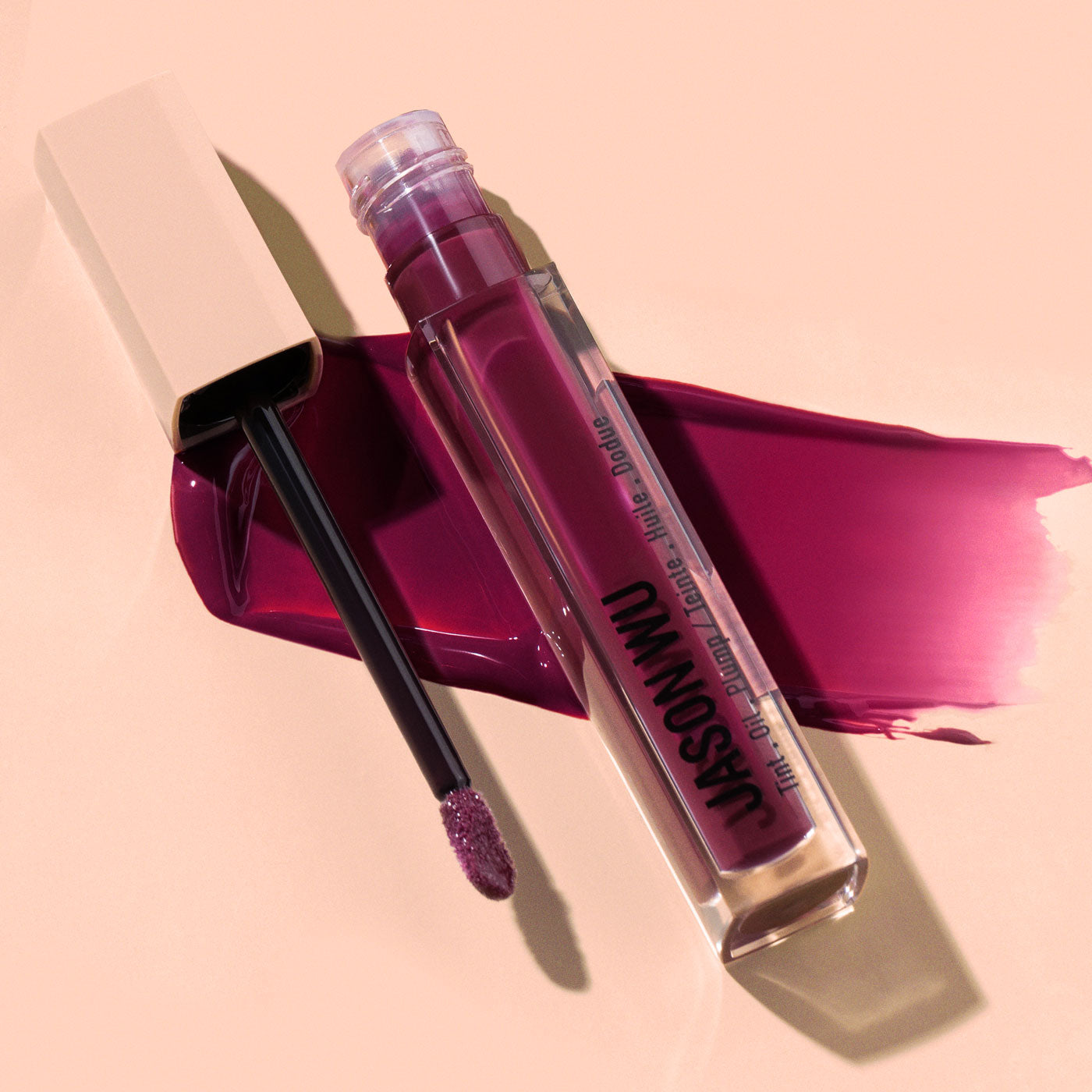 Open tube of dark pink liquid lipstick with applicator on a light background