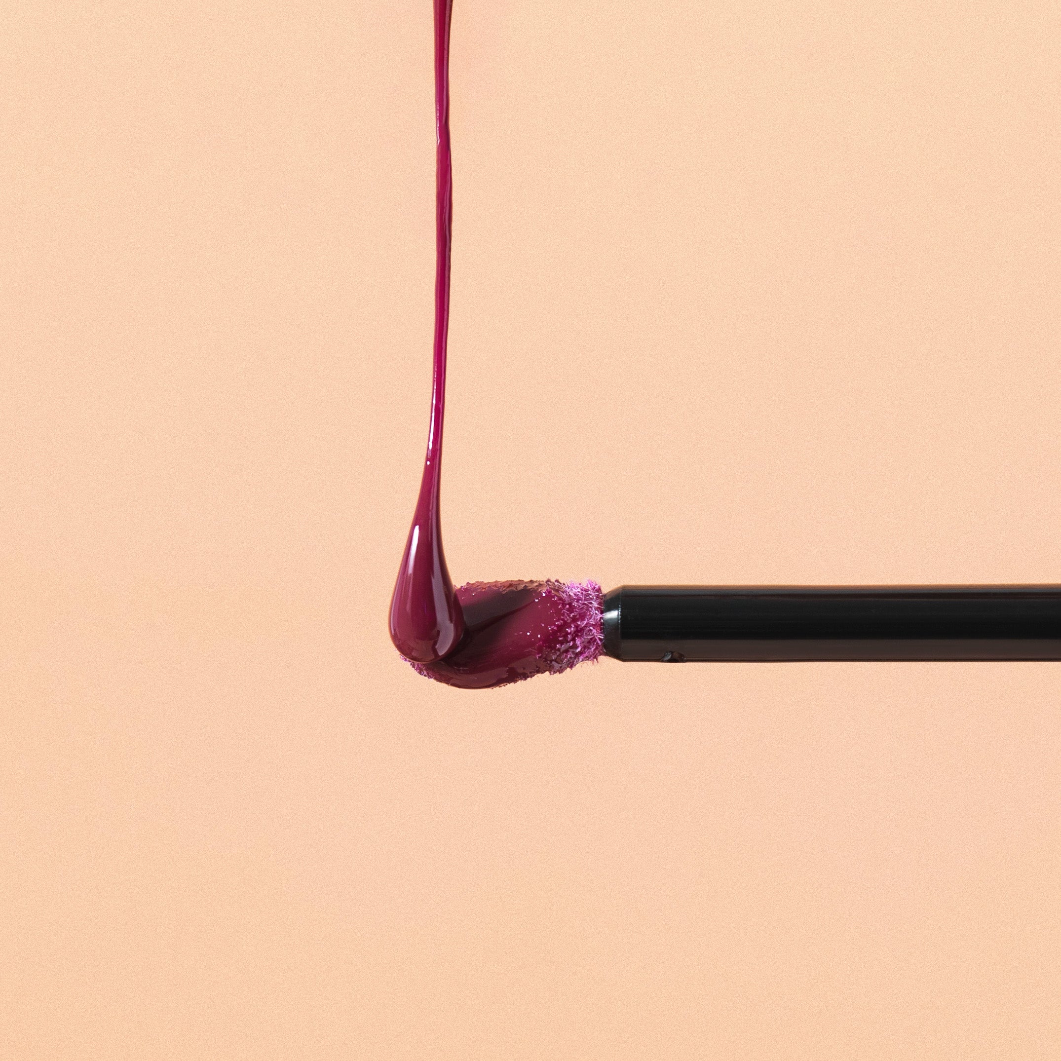 Close-up of a makeup brush applying a drop of red liquid