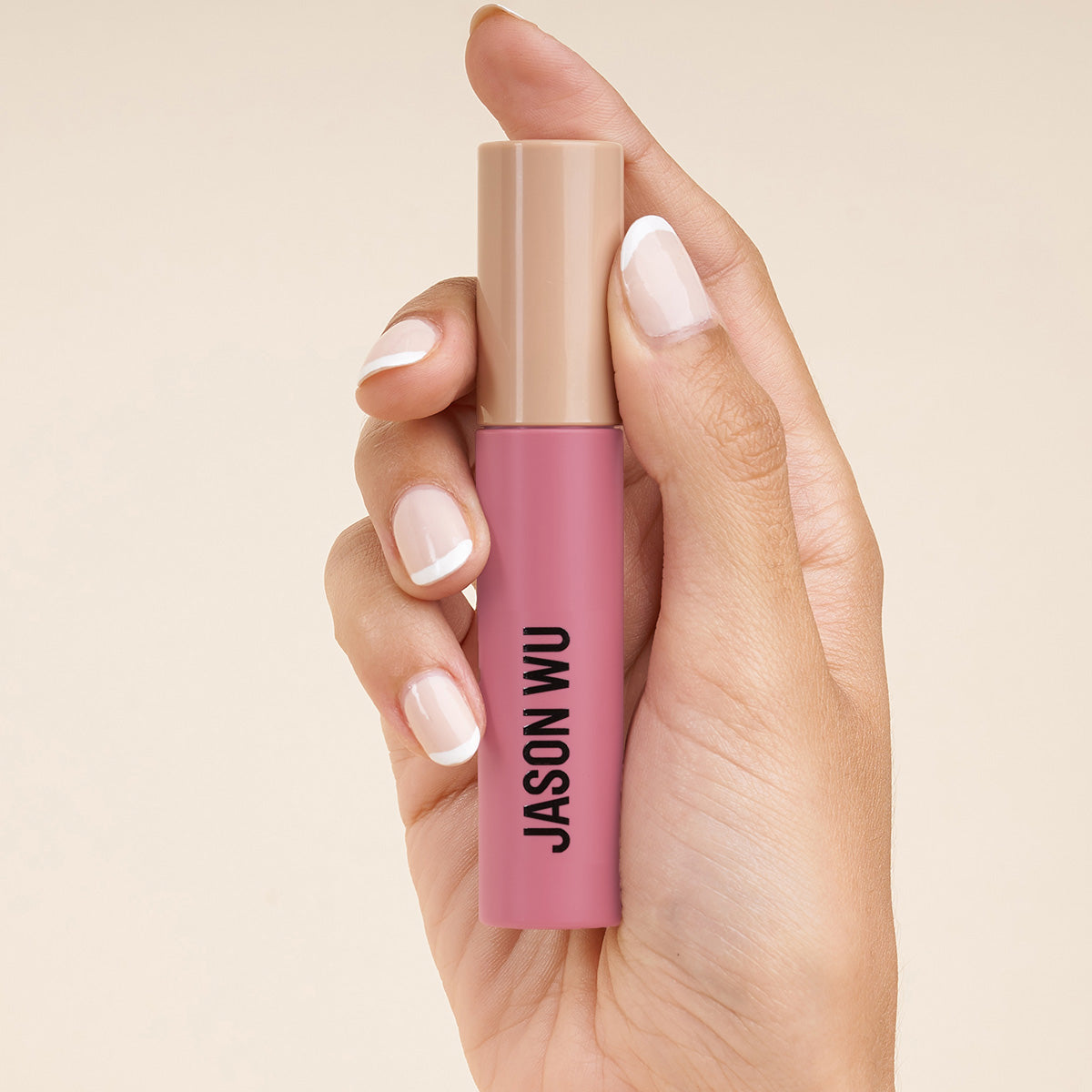 Hand holding a pink lipstick with beige cap