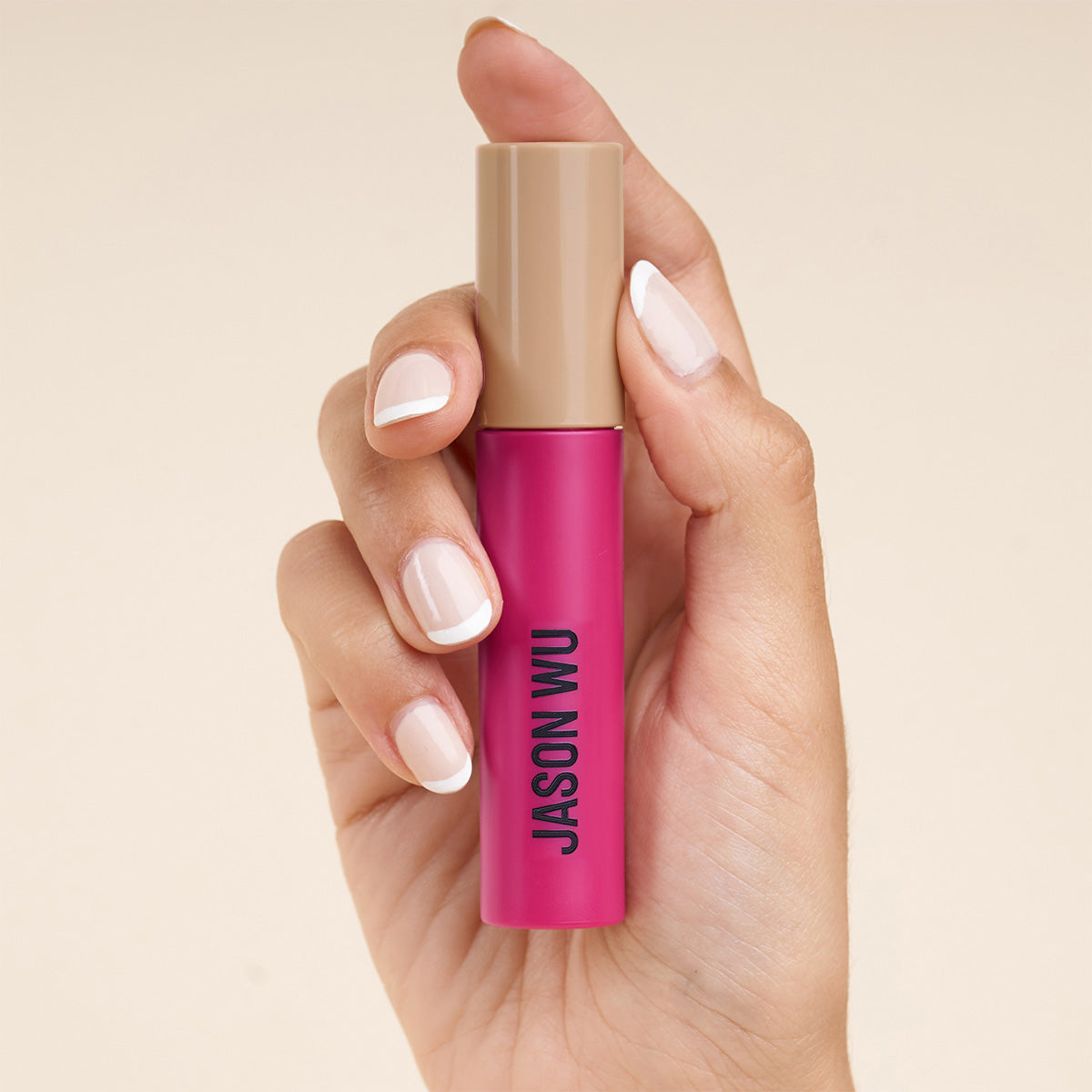 Hand holding a pink and beige lipstick tube