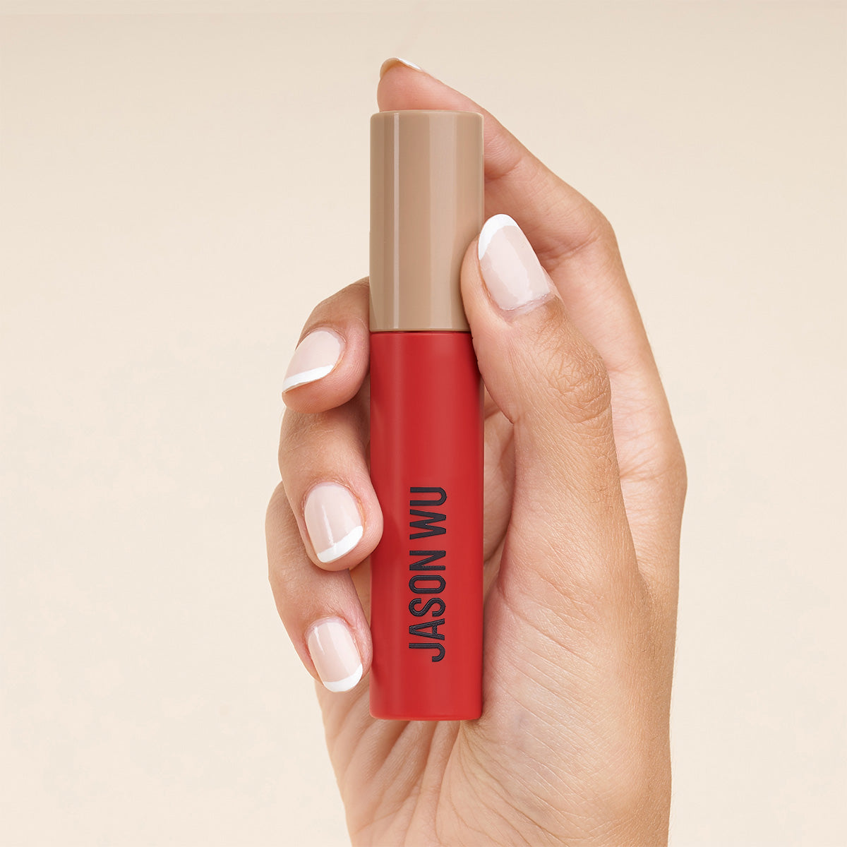 Hand holding a red and beige lipstick tube with text.