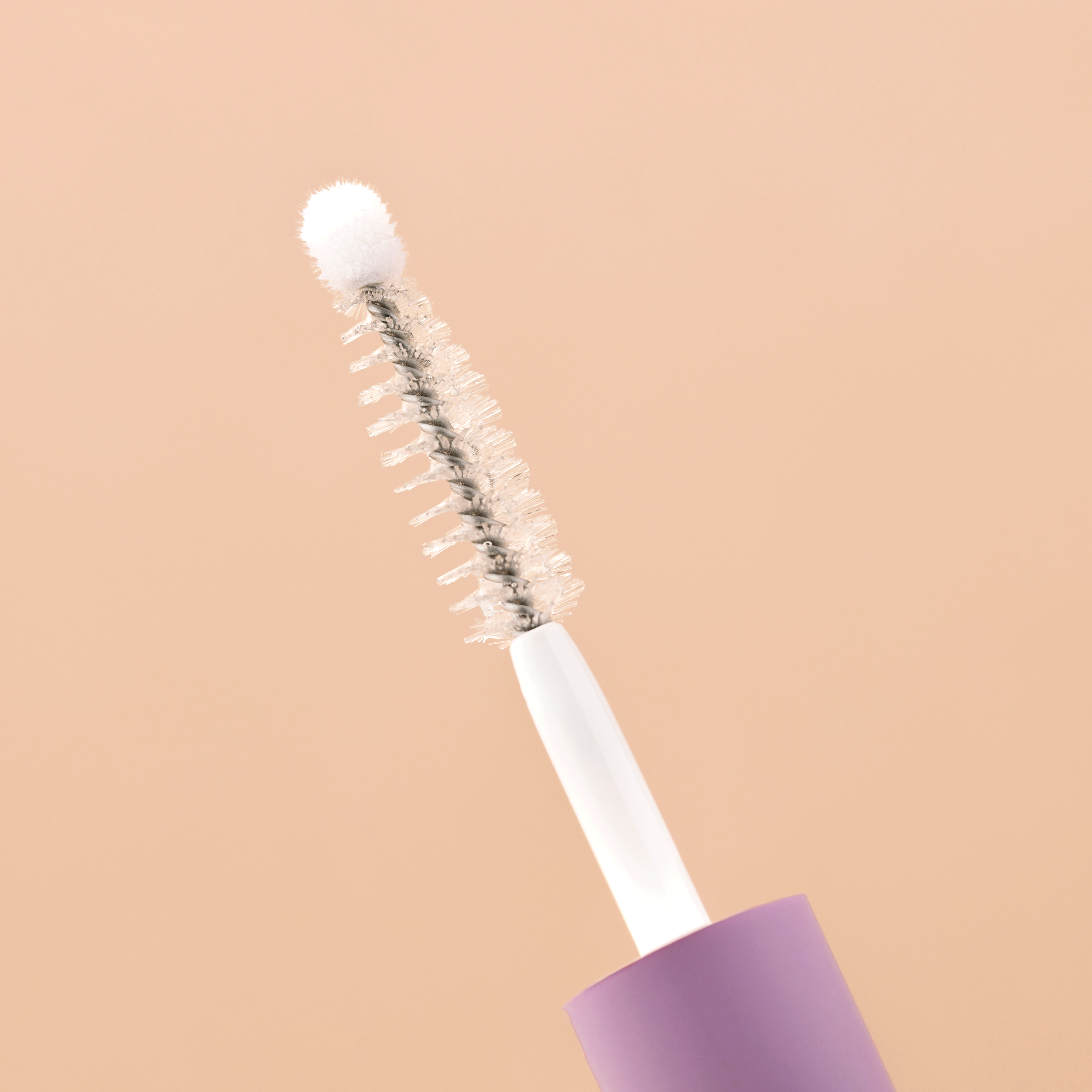 Close-up of a mascara wand against a beige background.